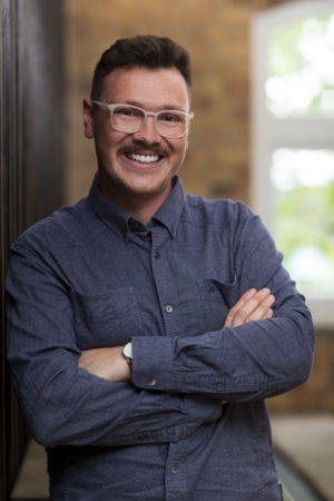 Environmental portrait of a man leaning against a wall in an Auckland industrial office setting