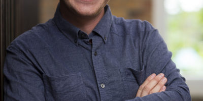 Environmental portrait of a man leaning against a wall in an Auckland industrial office setting