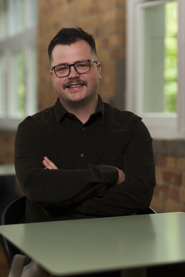 Environmental portrait of a man sitting at a table with window behind him