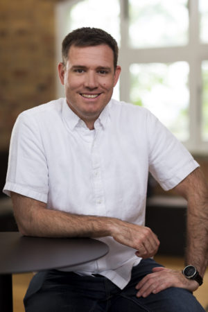 Environmental portrait of a man sitting at a table with window behind him