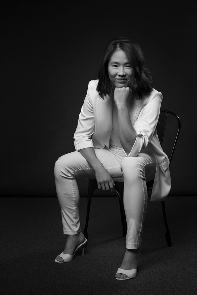 Studio photograph of young business woman sitting on a chair in front of a dark grey background