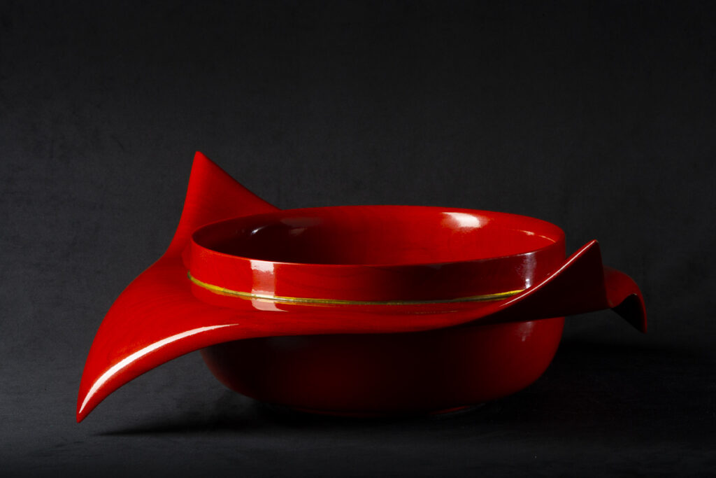 product photograph of red carved wooden bowl on a dark studio background