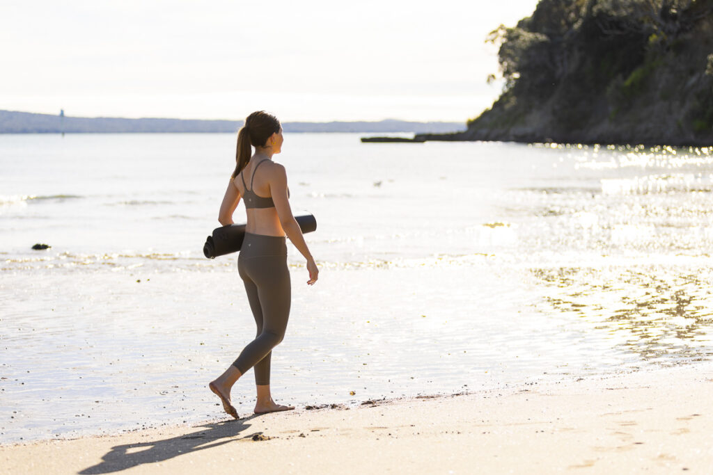 Woman walking along Saint Heliers beach with the sun behind her