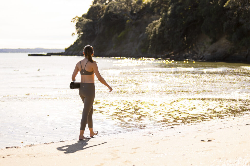 Woman walking along Saint Heliers beach with a yoga mat photographed by local professional photographer Adam Firth