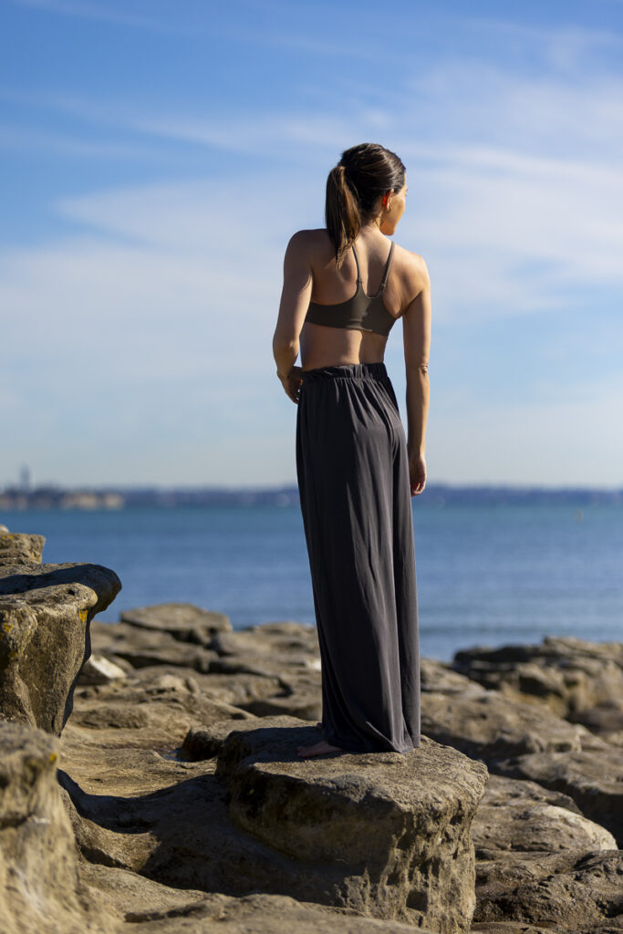 Photograph by portrait photographer Adam Firth at Saint Heliers beach in Auckland of a woman in yoga clothing on the local rocks in the morning sun.
