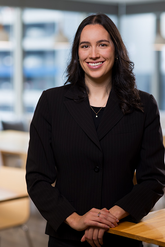 Environmental headshot of a young lady. Image has large windows in the background showing an out of focus Auckland city view