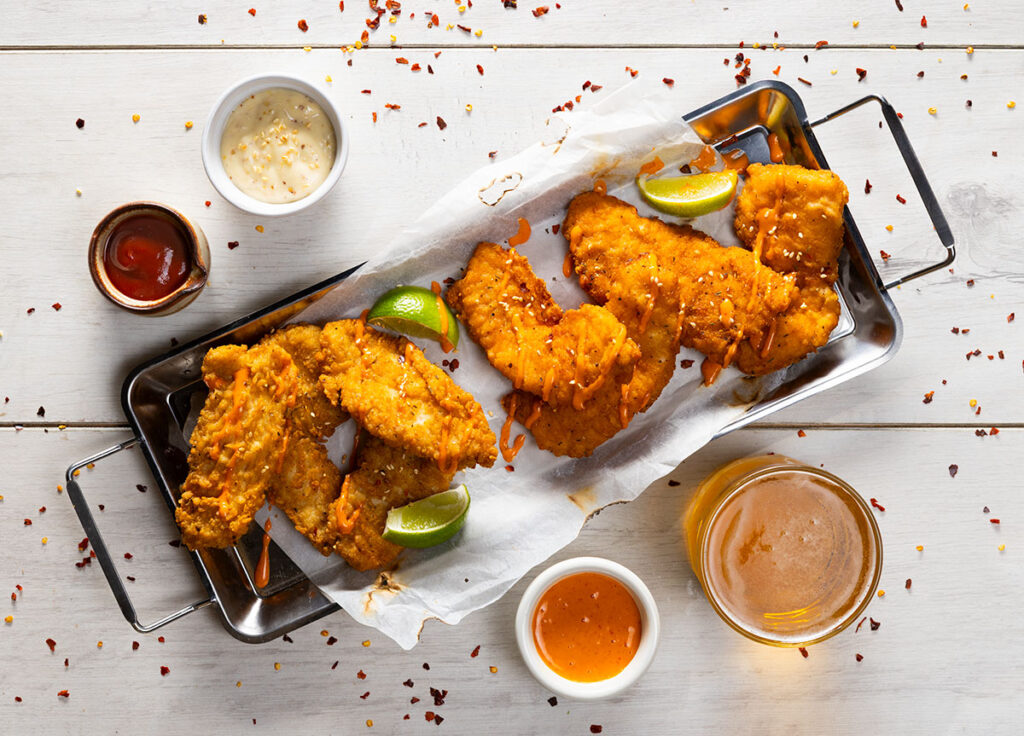 tray of fried chick photographed on a white background with scattered chilli and sauces